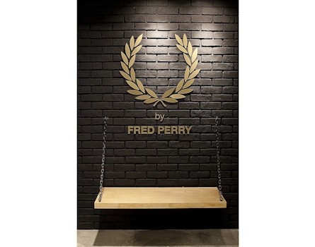 The Fred Perry Laurel Wreath Store in Singapore, designed by Studio Königshausen, pays homage to music and youth culture through its unique design. The exterior resembles a classic English shop front, while the window display resembles a vinyl record store with a Marantz vinyl player. Inside, a neon Laurel Wreath logo illuminates the space, and modular product walls house vinyl records alongside Fred Perry products for a distinct retail experience.